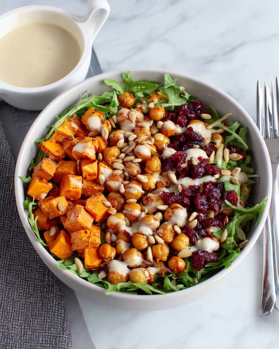 The image shows a bowl of salad with five layers. The first layer is fresh green arugula leaves spread evenly at the bottom. The second layer has golden-brown roasted chickpeas scattered over the greens. The third layer includes bright orange sweet potato cubes placed among the chickpeas. The fourth layer is sprinkled with small red dried cranberries and light brown sunflower seeds all over the top. The final layer is drizzled with a creamy light beige dressing. The white bowl is on a white marbled surface, next to a white bowl filled with extra dressing, and a fork lies beside the bowl. Photo taken with an iphone --ar 4:5 --v 7
