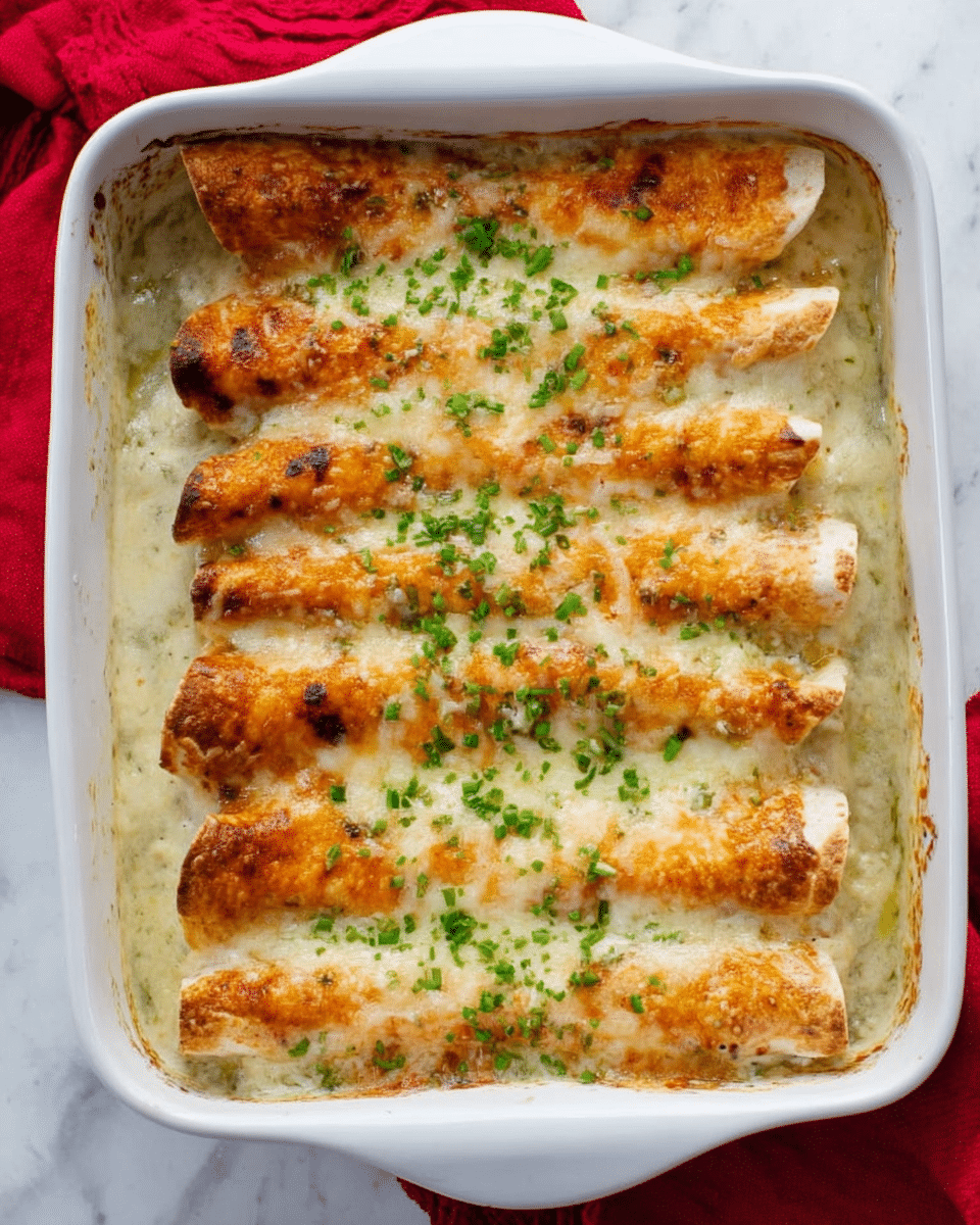 The image shows a white baking dish filled with five rolled enchiladas placed side by side, covered in a creamy white sauce and melted cheese. The enchiladas have a slightly browned, golden-baked top layer with melted gooey cheese bubbling around the edges. Chopped green herbs are sprinkled evenly over the top, adding a touch of fresh green color. The background features a white marbled surface with a red cloth on the side. Photo taken with an iphone --ar 4:5 --v 7