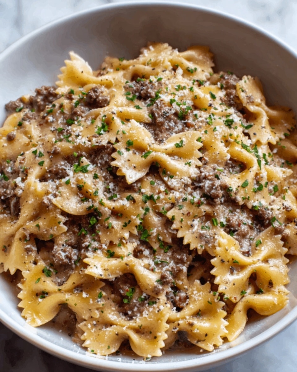 The image shows a white bowl filled with about three layers of bow-tie pasta mixed with ground beef. The top layer of pasta is light yellow with a smooth texture, scattered evenly across the bowl. Between and on top of the pasta, there are small pieces of cooked ground beef in a brown color, adding a rough texture contrast. The dish is topped with a light tan sauce that coats the pasta and meat, and small green herbs are sprinkled lightly over the surface for a pop of color. The dish rests on a white marbled surface. Photo taken with an iphone --ar 4:5 --v 7