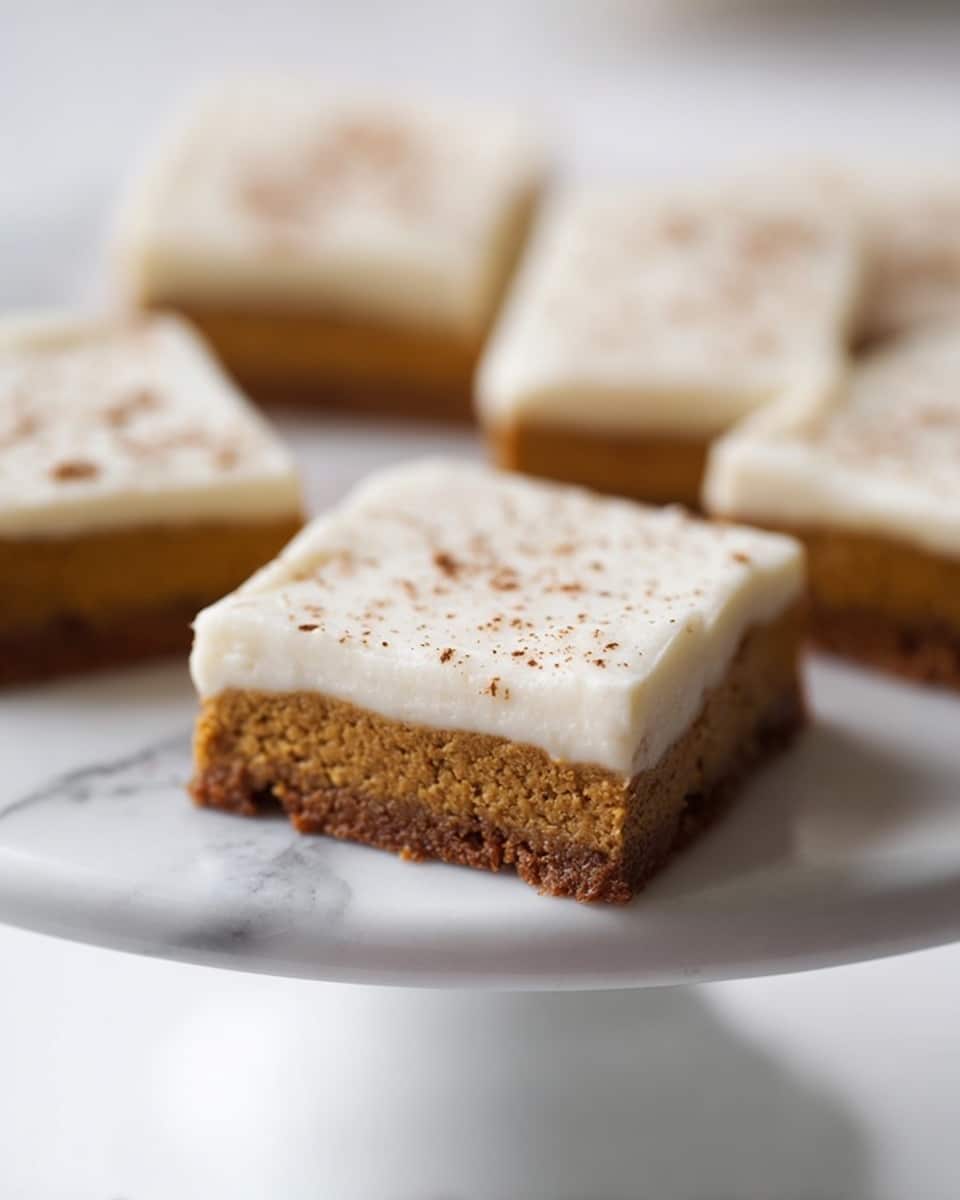 The image shows several square dessert bars on a white cake stand with a white marbled surface. Each bar has two layers: a bottom layer that is dense, brown, and slightly textured, and a thick, smooth top layer that is off-white and creamy. The top layer is sprinkled lightly with small brown powder spots, possibly cinnamon or cocoa. The bars are evenly cut and arranged with one piece in the foreground clearly in focus, while the others are blurred in the background. photo taken with an iphone --ar 4:5 --v 7